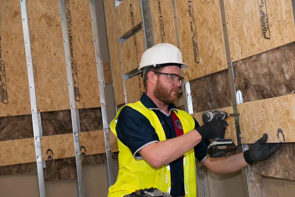 man in hard hat and hi vis jacket drilling in to MDF